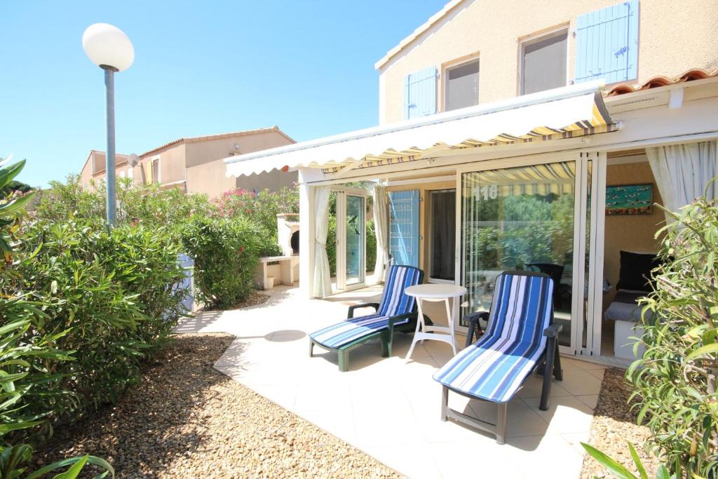 un patio avec deux chaises bleues et une table dans l'établissement Belle villa d angle avec veranda et WIFI, 2 chambres dans résidence sécurisée avec piscine commune 800m de la mer Un vrai Havre de Paix LRCS116, à Portiragnes