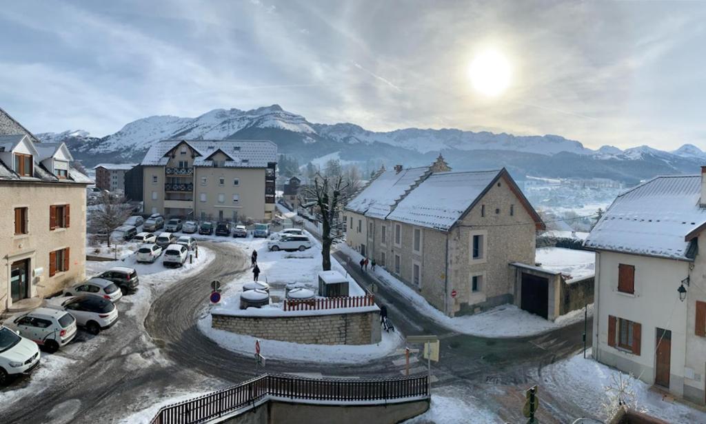 een stad met besneeuwde gebouwen en geparkeerde auto's bij Appartement centre village in Villard-de-Lans