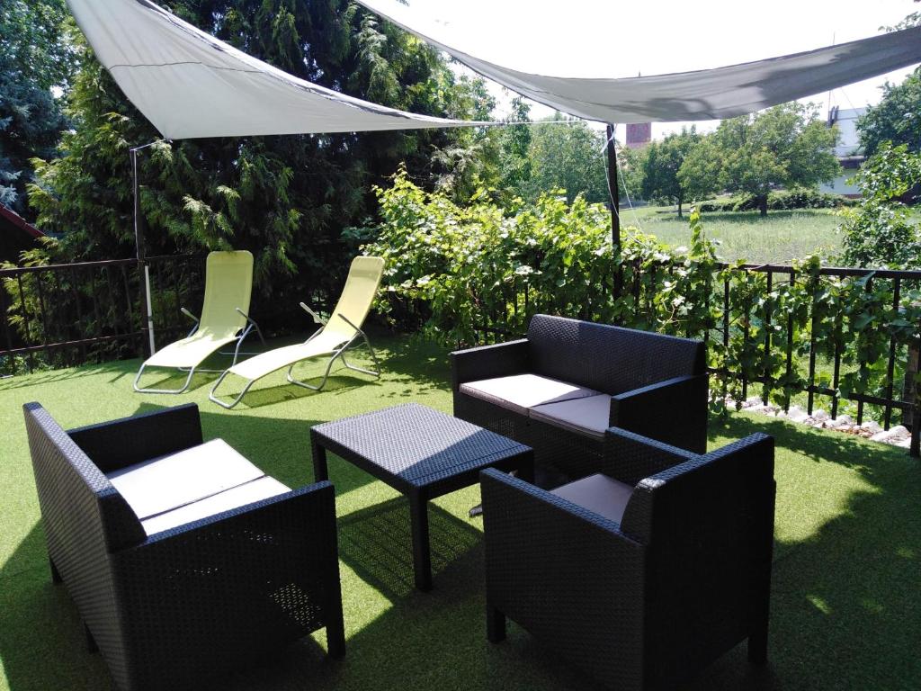 eine Terrasse mit Stühlen, Tischen und einem weißen Sonnenschirm in der Unterkunft Háromfenyő Apartman in Révfülöp