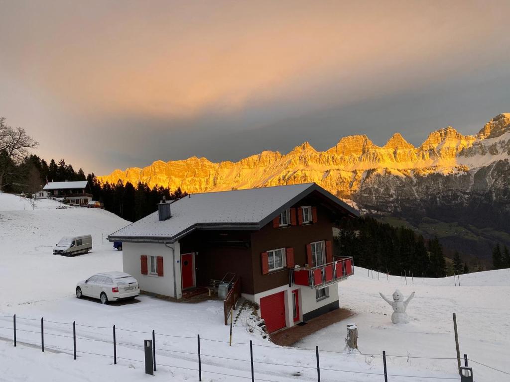 a house with a car parked in the snow with mountains at Ferienwohnung Tschudiboden in Flumserberg