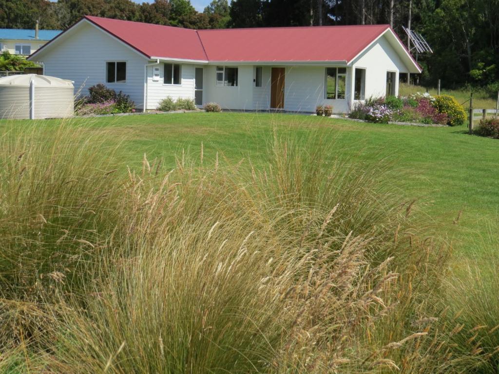 a white house with a red roof and a field of grass at waikawa house in Niagara