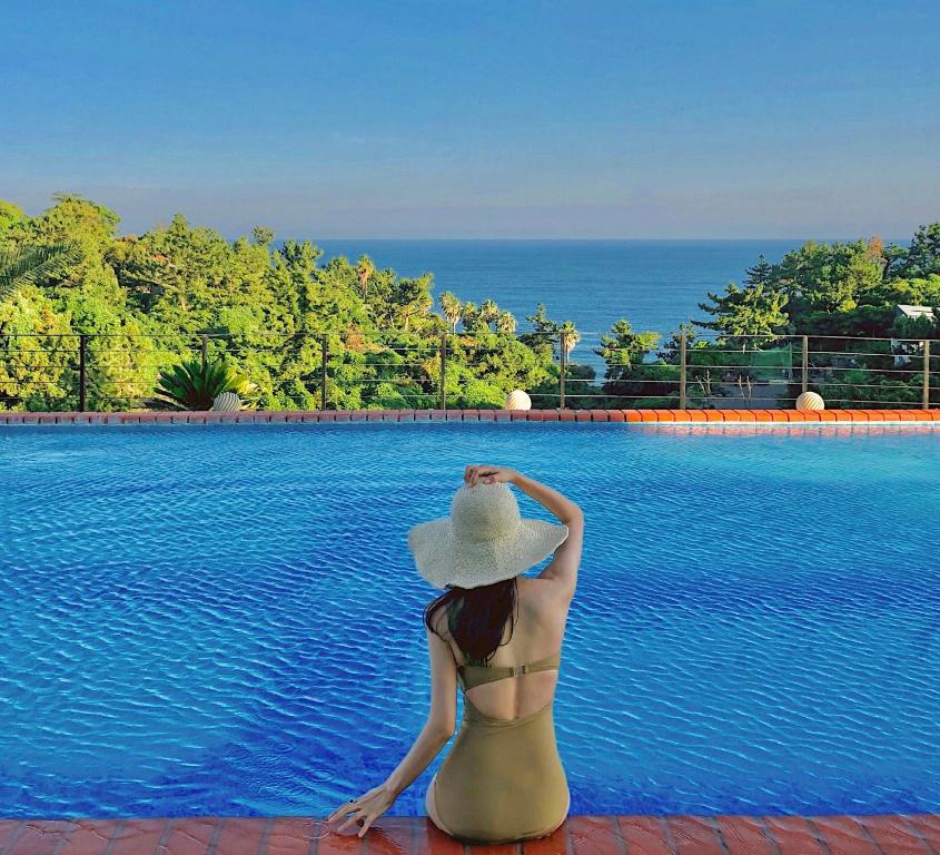 a woman in a bikini and hat sitting next to a swimming pool at GoldOne Hotel & Suites in Seogwipo