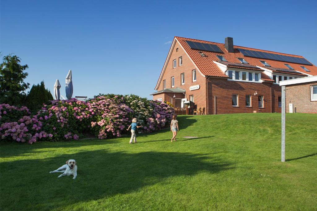 two people and a dog in the grass in front of a house at Hotel Hus Achtern Diek in Insel Neuwerk