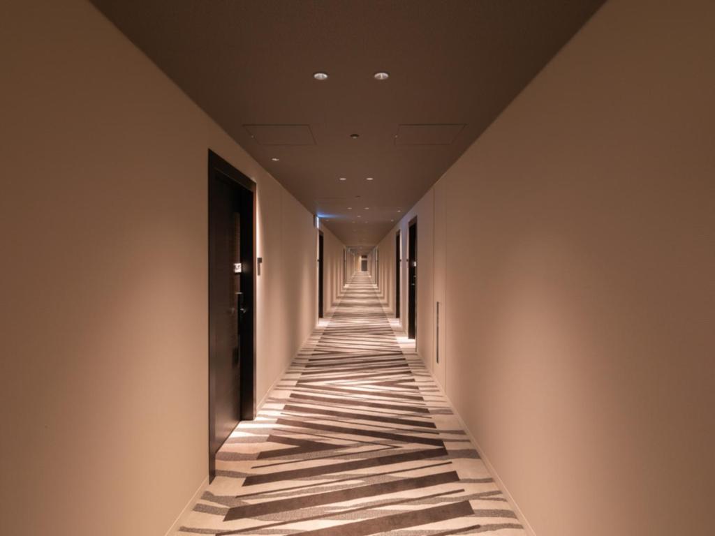 an empty hallway with a long corridor with lights on the walls at LIBER HOTEL Osaka in Osaka
