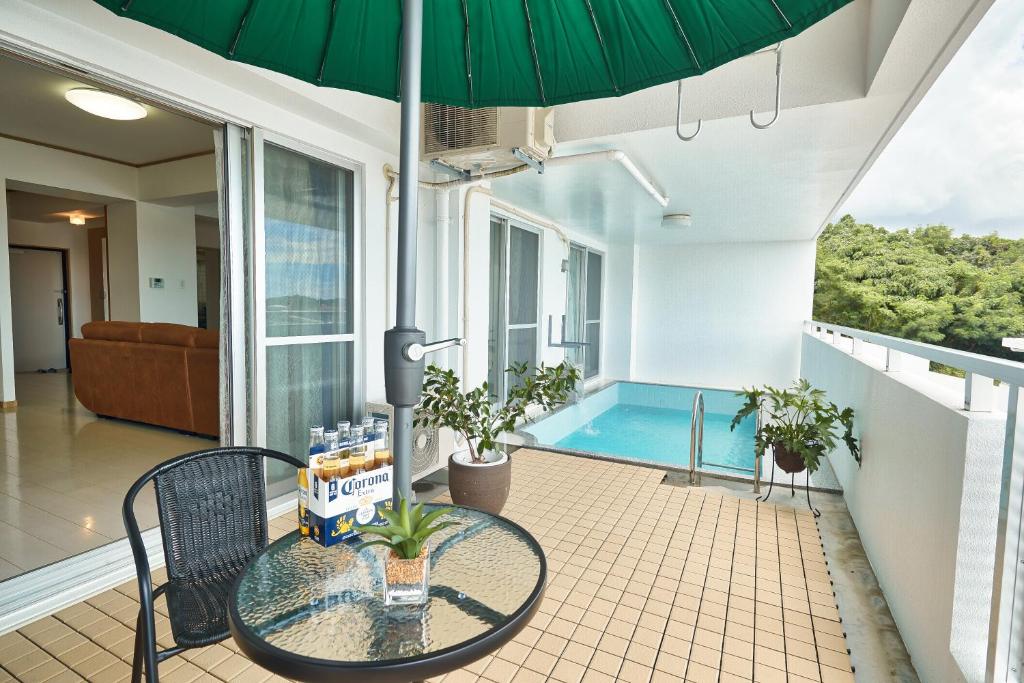 eine Terrasse mit einem Tisch, einem Sonnenschirm und einem Pool in der Unterkunft FreedomHillsフリーダムヒルズA棟 in Tomigusuku