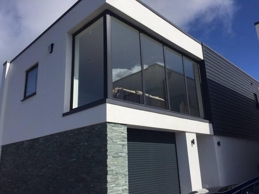 a house with large windows on the side of it at Relax in style at my stunning Holywell Beach home in Holywell Bay