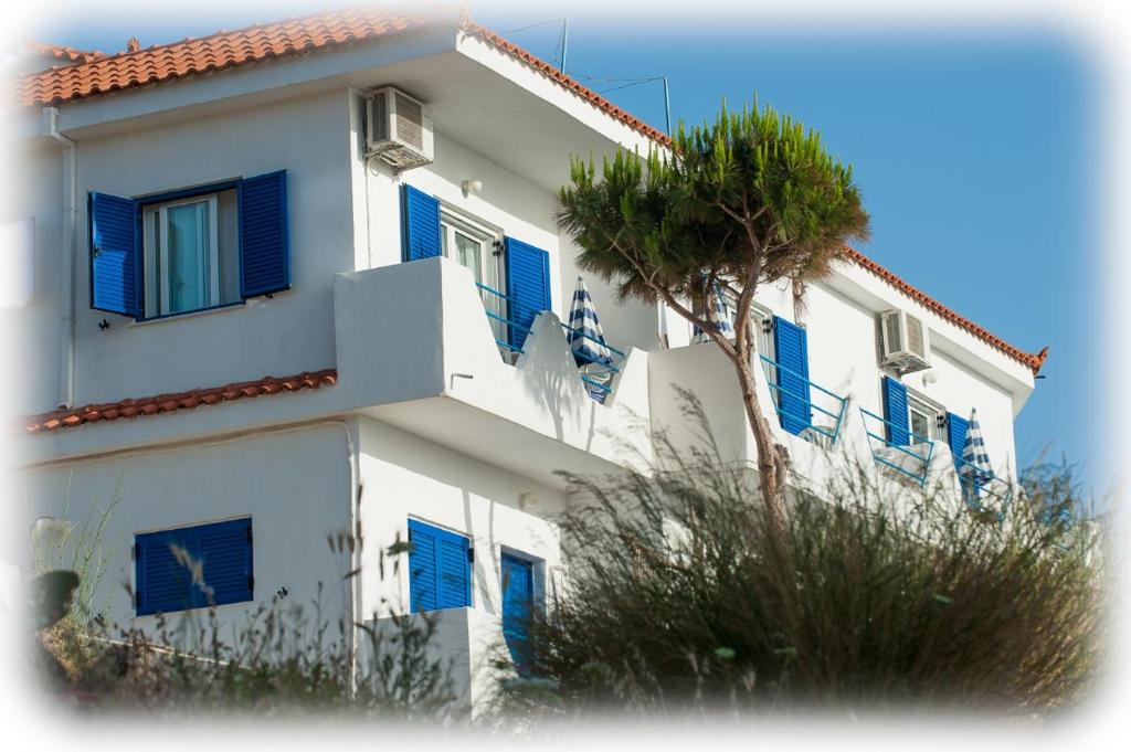 a white building with blue windows and a palm tree at Haris Apartments in Armenistis