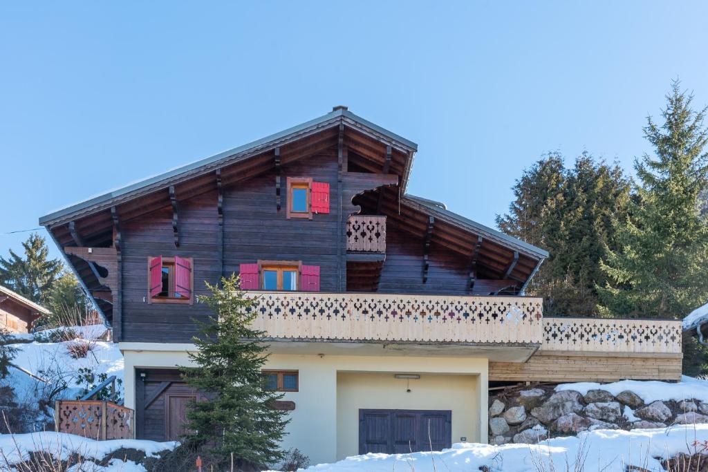 Une grande maison en bois avec des fenêtres rouges dans la neige dans l'établissement Chalet Mahana, aux Gets