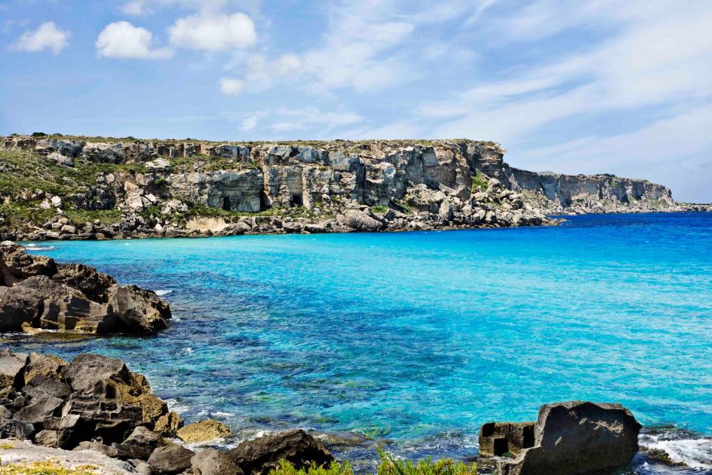 a beach with blue water and a rocky cliff at Luxmarì Hotel & Spa in Castellammare del Golfo