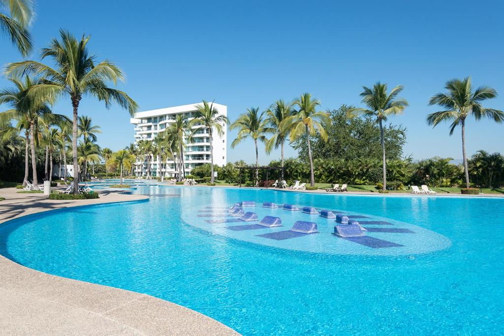 a large swimming pool with chaise lounges and palm trees at Condo en Nuevo Vallarta con acceso a playa in Mezcales