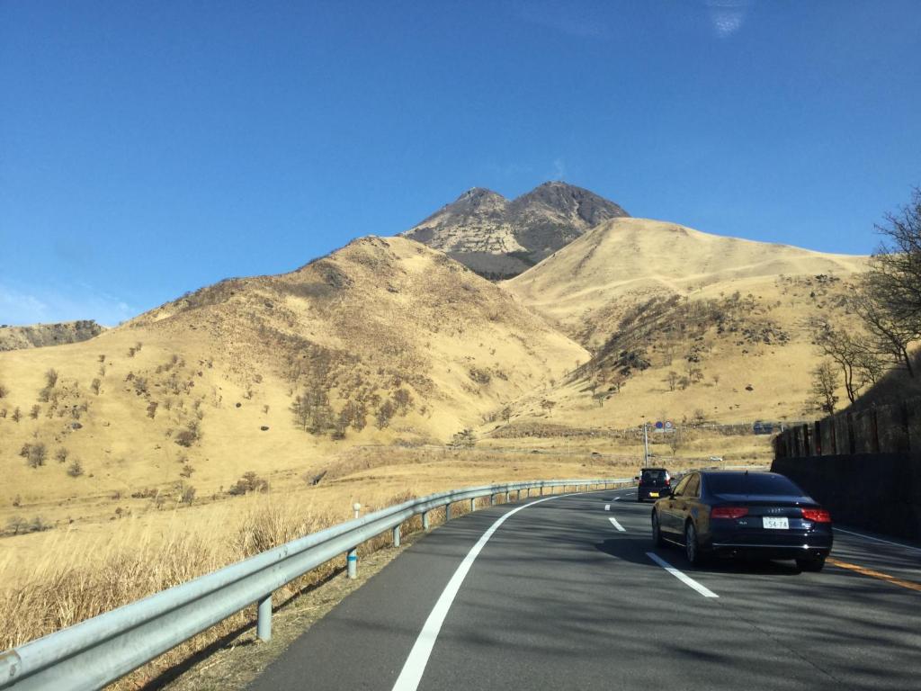 a car driving down a highway with mountains in the background at 湯布院月灯り in Yufuin