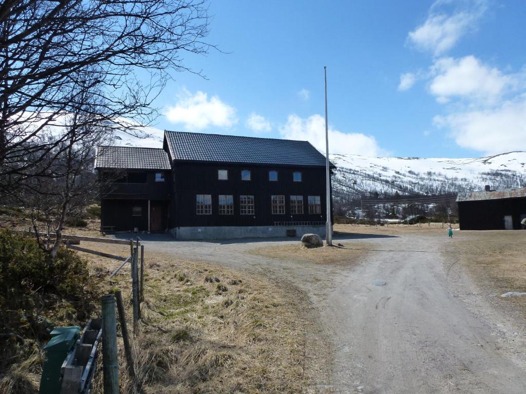 een zwart gebouw op een onverharde weg met een besneeuwde berg bij Jønndalen Høyfjellseter in Uvdal