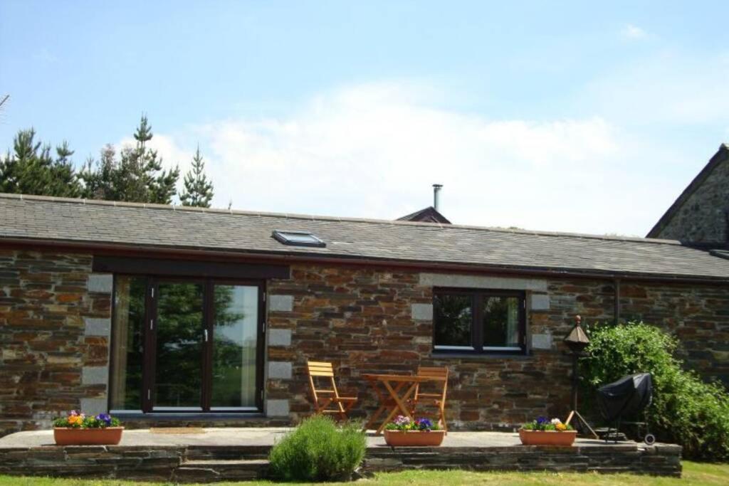 Ce cottage en pierre dispose de portes coulissantes en verre et d'une terrasse. dans l'établissement Wilson Cottage Dartmoor, à Tavistock