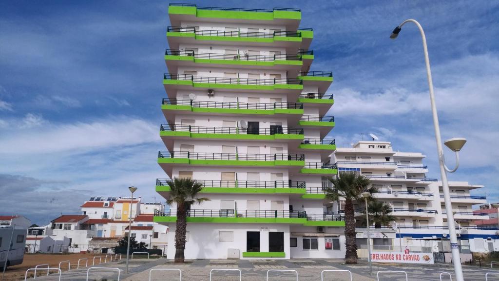 a tall building with palm trees in front of it at Monte Gordo T2 Frente Mar in Monte Gordo