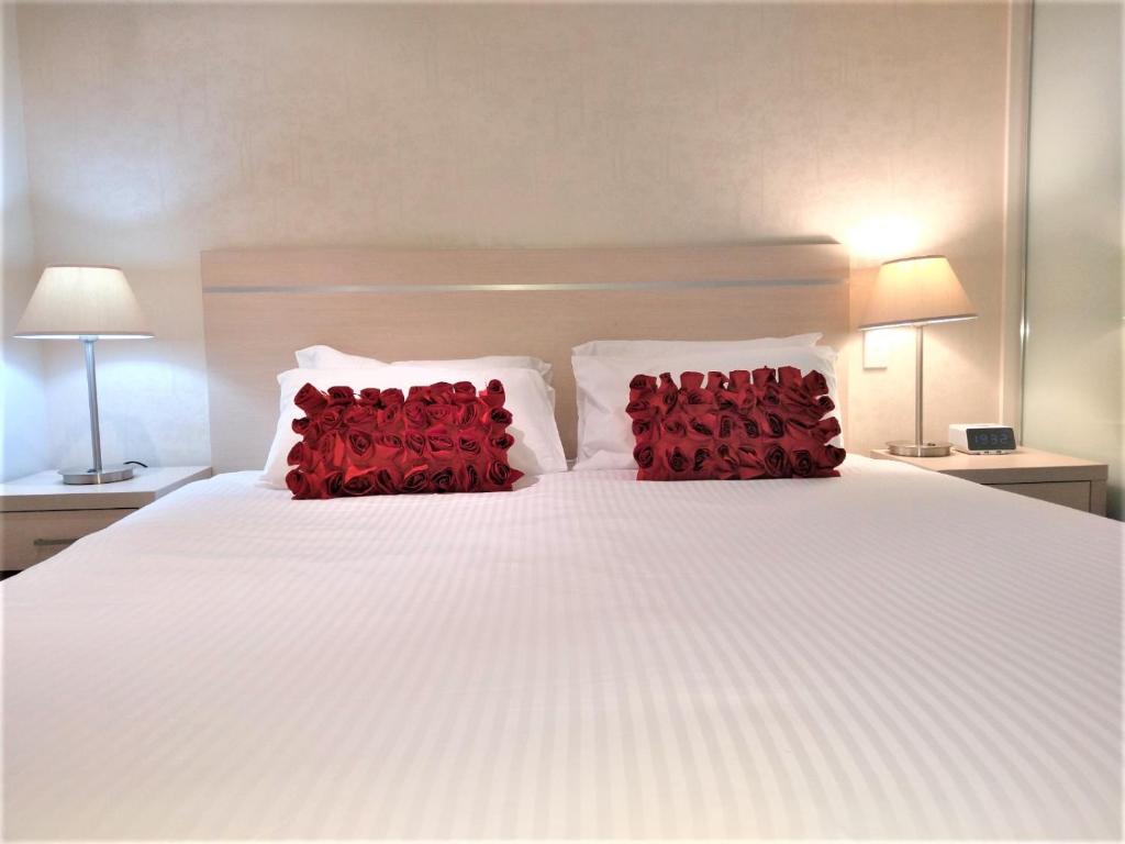 a white bed with two red pillows on it at Hi 5 star luxury Adelaide City Apartment in Adelaide