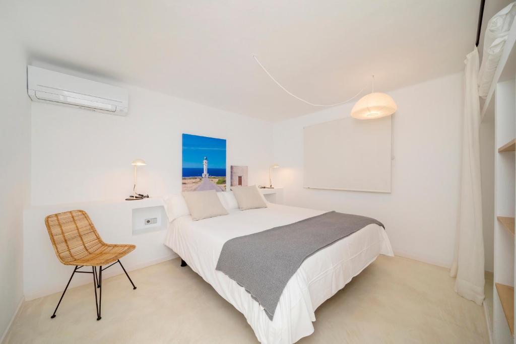 a white bedroom with a bed and a chair at Apartamentos Roca Plana in Es Pujols