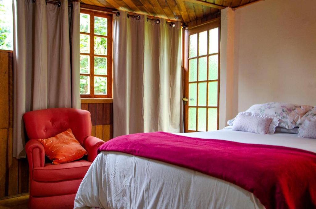 - une chambre avec un grand lit et une chaise rouge dans l'établissement Chalés Luz da Montanha, à Núcleo Mauá