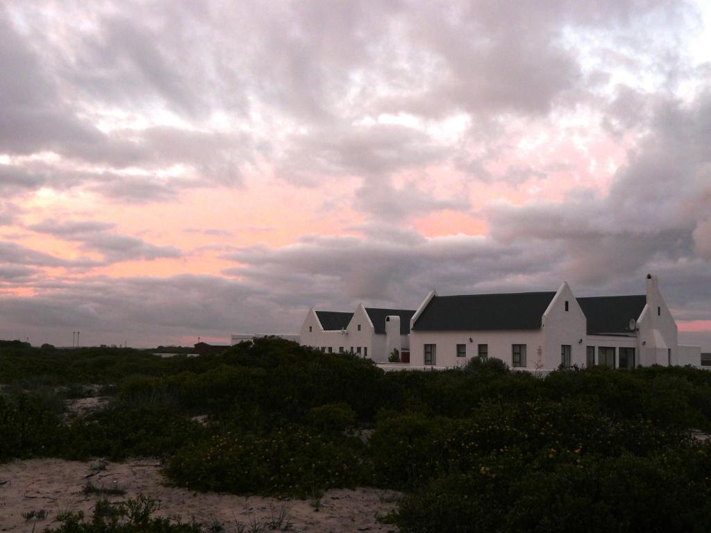 une maison blanche sur la plage avec un ciel nuageux dans l'établissement Jubel n Juig Self Catering, à Dwarskersbos