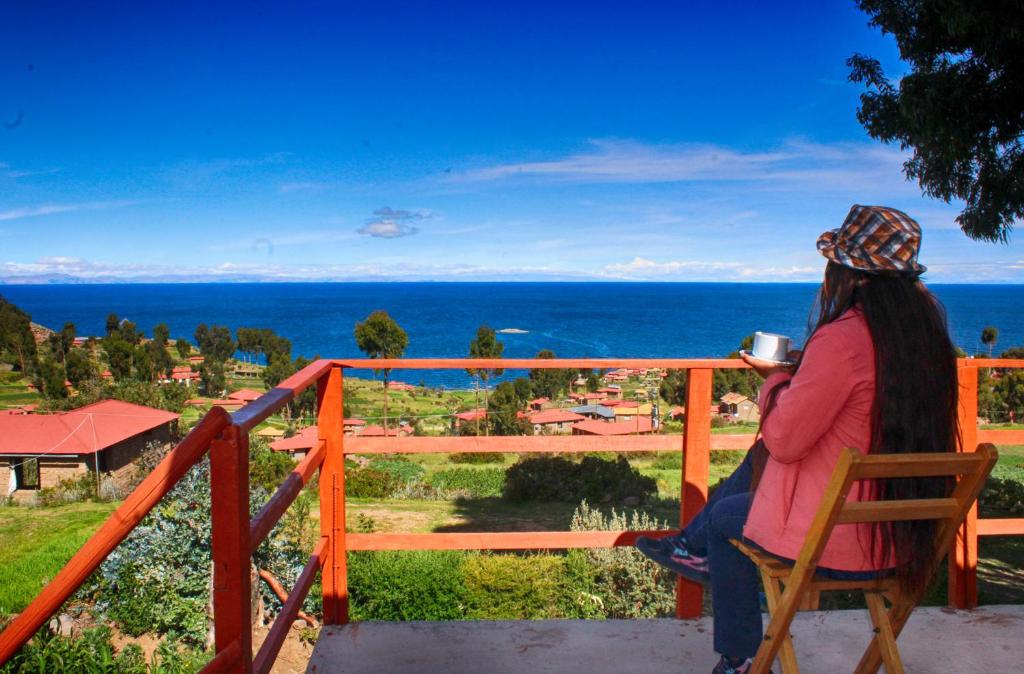 Eine Frau, die auf einem Stuhl sitzt und eine Tasse Kaffee trinkt. in der Unterkunft Inca lodge - Amantani in Ocosuyo