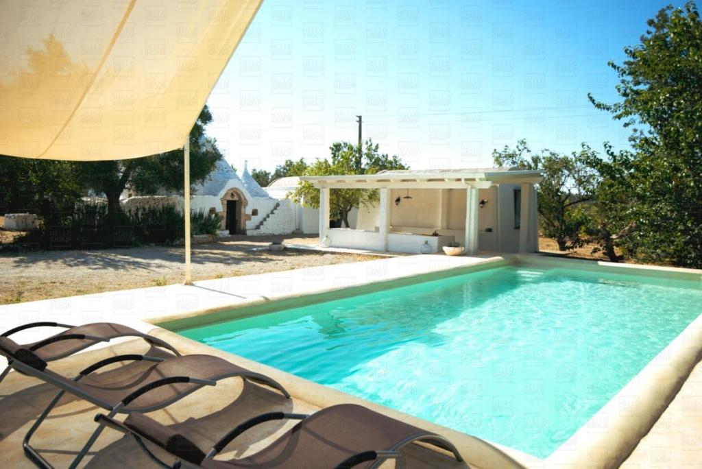 una piscina con due sedie e un ombrellone di HelloApulia - Enchanting Trulli del Mandorlo a Ceglie Messapica