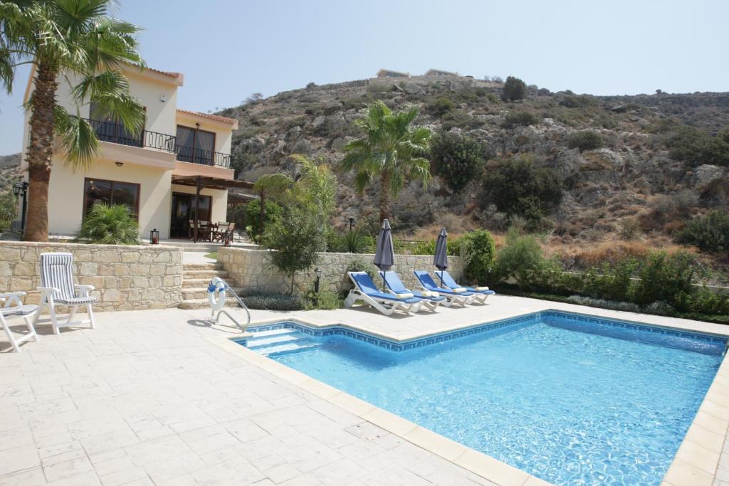 a villa with a swimming pool and two lawn chairs at Holidays Villas in Pissouri