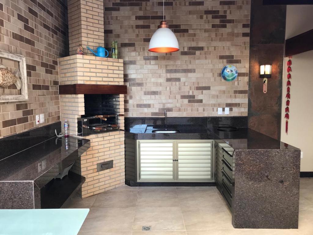 a kitchen with black counters and a brick wall at Apartamento com área externa na Bacutia - uma quadra do mar in Guarapari