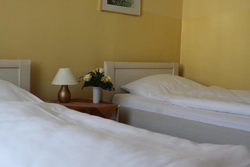 two beds in a bedroom with a lamp and flowers at Hotel Weile in Weiden