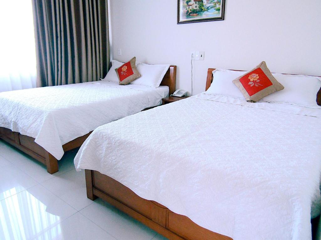 a bedroom with two beds with white sheets and red pillows at Hoang Dat Hotel in Dong Hoi