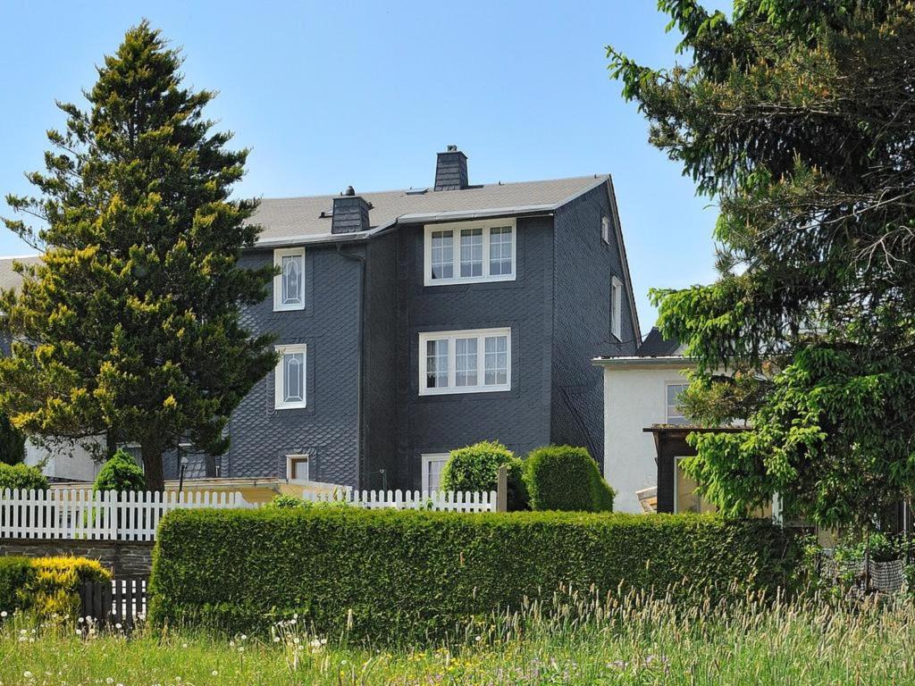 una casa negra con una cerca blanca y un árbol en Ferienwohnung "An den Kurwiesen", en Masserberg