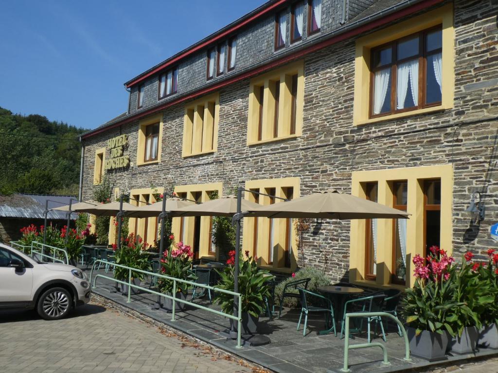 ein Gebäude mit Tischen und Sonnenschirmen davor in der Unterkunft Hotel Des Roches in Cugnon