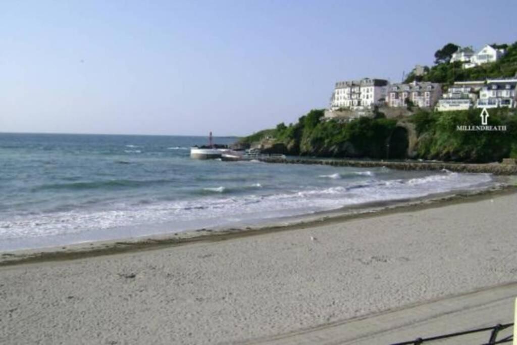 a beach with houses on a hill next to the ocean at Millendreath at Westcliff - Self Catering flat with amazing sea views in Looe