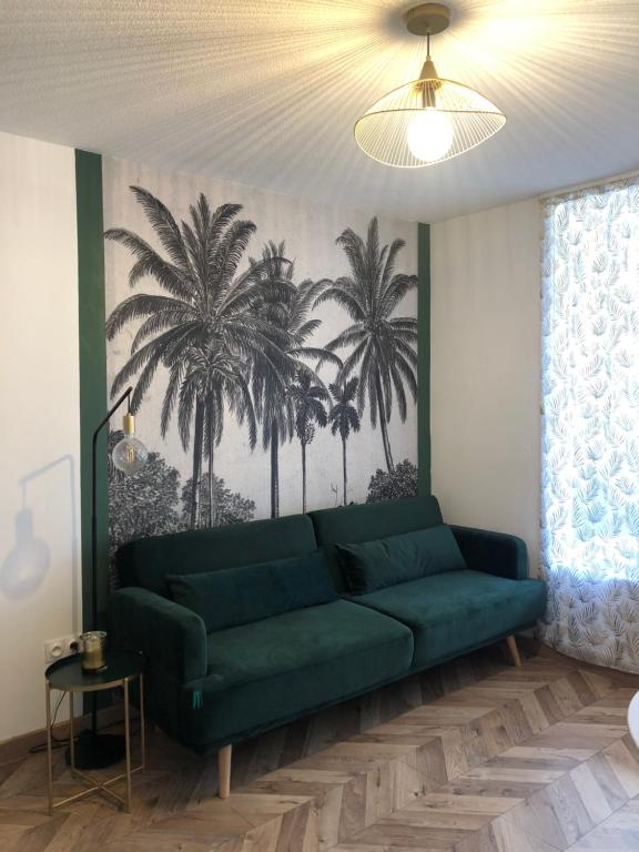 a green couch in a living room with palm trees on the wall at Les Palmiers de Gruissan, T2, Vue Port ! in Gruissan
