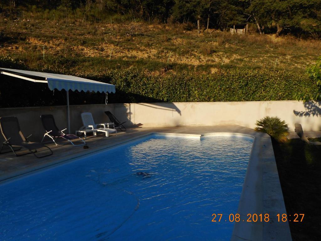 a blue swimming pool with chairs and an umbrella at LES TILLEULS in Riez