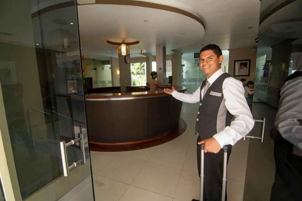 un hombre con chaleco y corbata parado junto a un bar en El Dorado Classic Hotel en Iquitos