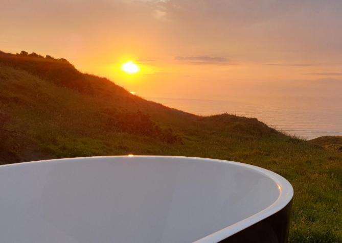 a bath tub with the sunset in the background at SeaView Retreat -Amazing Ocean Views and Outdoor bath in Waiuku