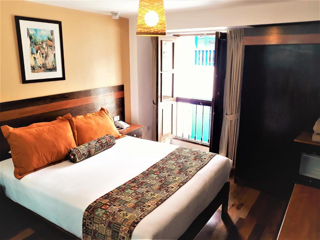 1 dormitorio con 1 cama con almohadas de color naranja y ventana en Posada San Blas en Cuzco