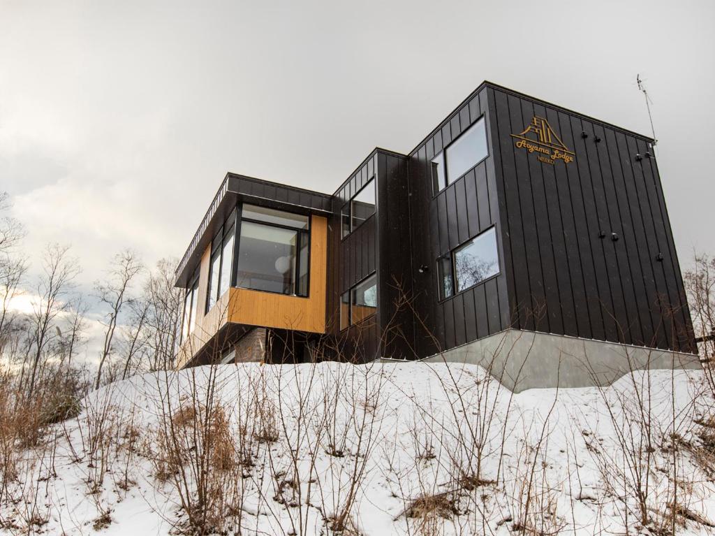 a black house on top of a hill in the snow at Aoyama Lodge in Niseko