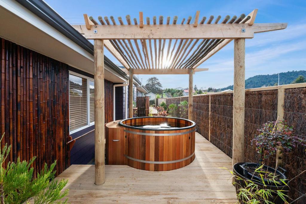 una terraza de madera con bañera de hidromasaje bajo una pérgola en The Purple House - Ohakune Home with Spa Pool en Ohakune
