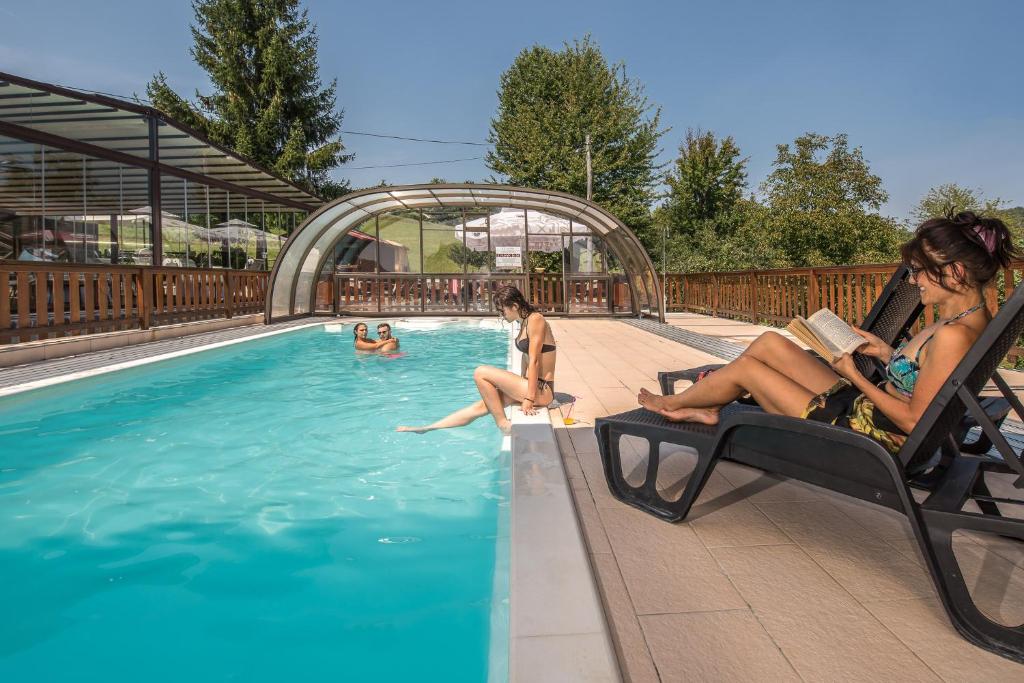 a woman sitting in a chair reading a book in a swimming pool at Hotel Srakovcic Heart of Nature in Ribnik