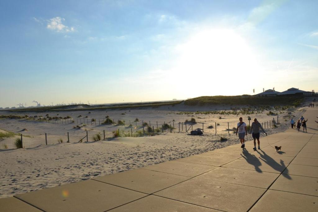 dos personas caminando por una acera en la playa en 6p Luxe bungalow met serre en 's-Gravenzande