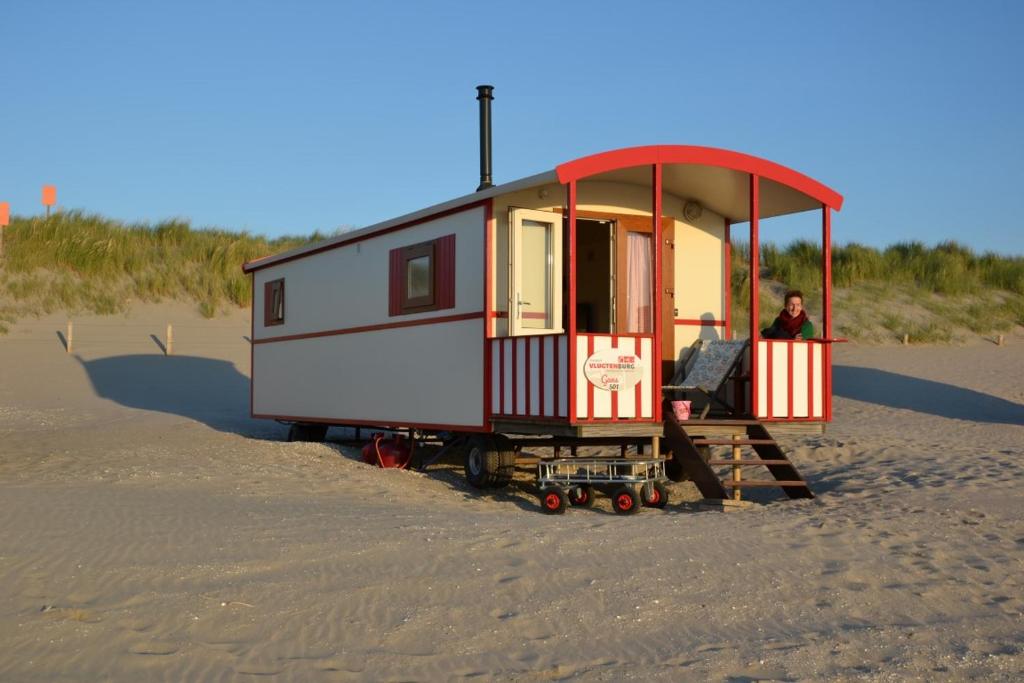 a small house on the beach with a man sitting in it at Pipowagen op het strand in s-Gravenzande