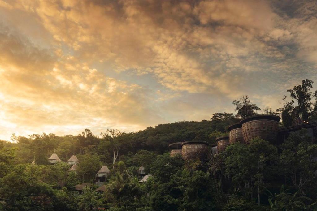 einen wolkigen Himmel mit Bäumen und Häusern auf einem Hügel in der Unterkunft Keemala in Kamala Beach