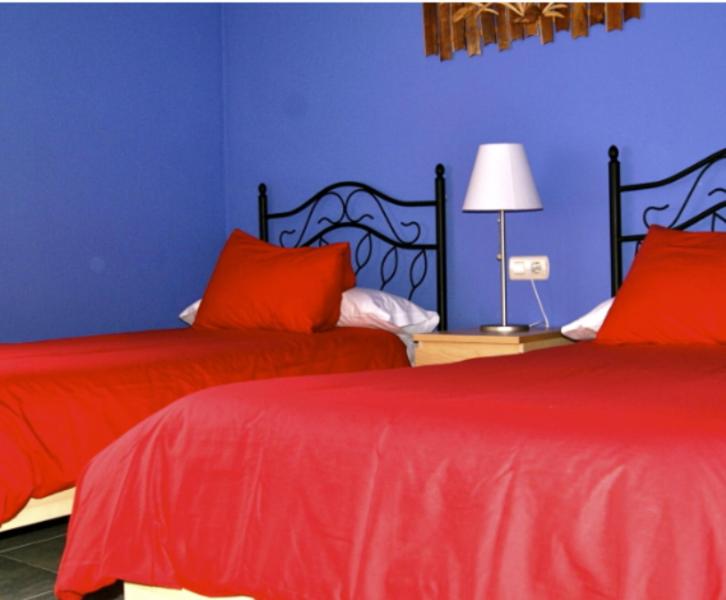 1 dormitorio con 2 camas con sábanas rojas y pared azul en Apartamentos El Castañar, en Hervás