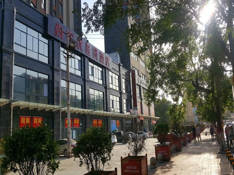 a building on a city street with trees and buildings at Thank Inn Chain Hotel Shanxi xianyang train station in Xianyang