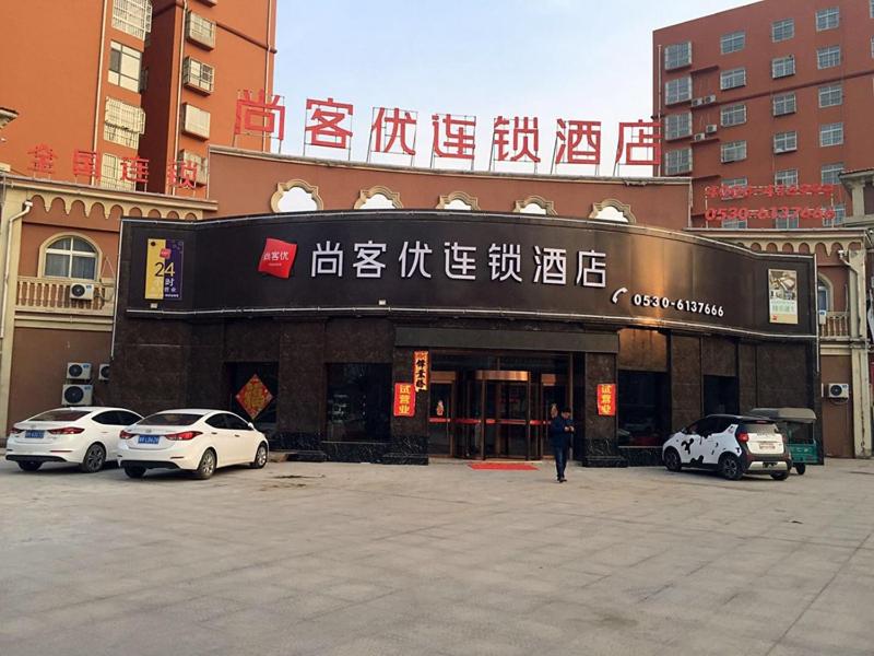 um edifício com carros estacionados num parque de estacionamento em Thank Inn Chain Hotel shandong heze juye county shanghai jiayuan em Heze