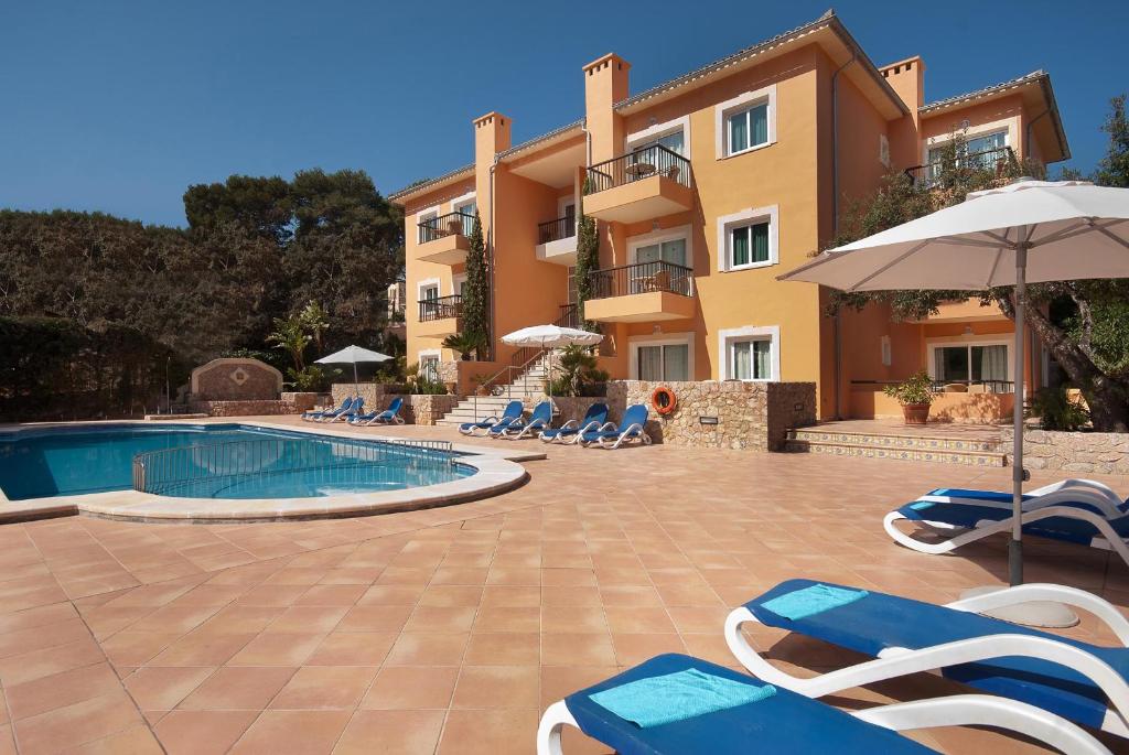 a resort with a swimming pool with chairs and an umbrella at PINOS ALTOS 04 in Cala de Sant Vicenc