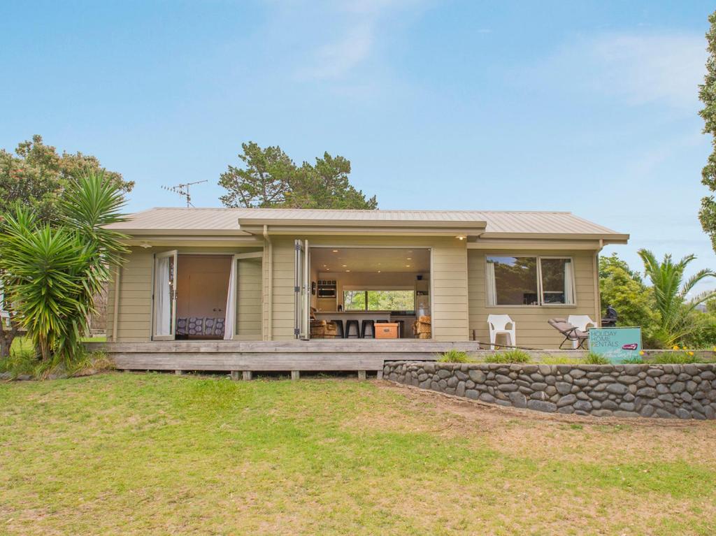 une maison avec une grande terrasse couverte et un mur en pierre dans l'établissement On The Green - Pauanui Holiday Home, à Pauanui