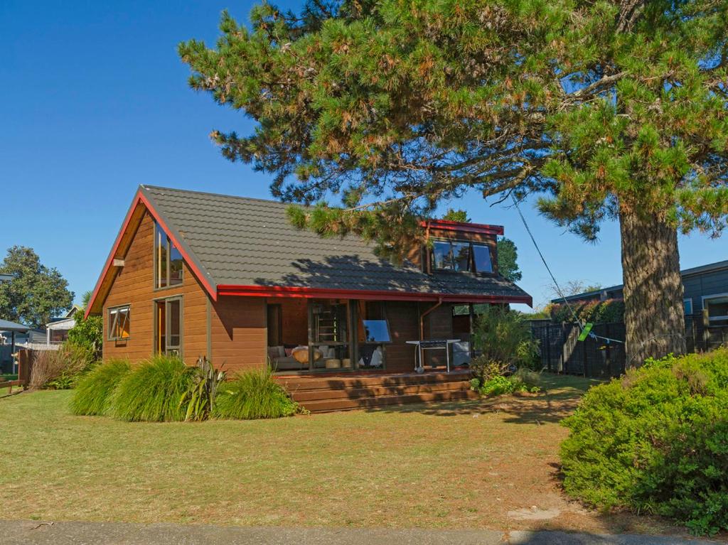 a brown house with a red roof and a tree at Estuary Escape - Pauanui Holiday Home in Pauanui