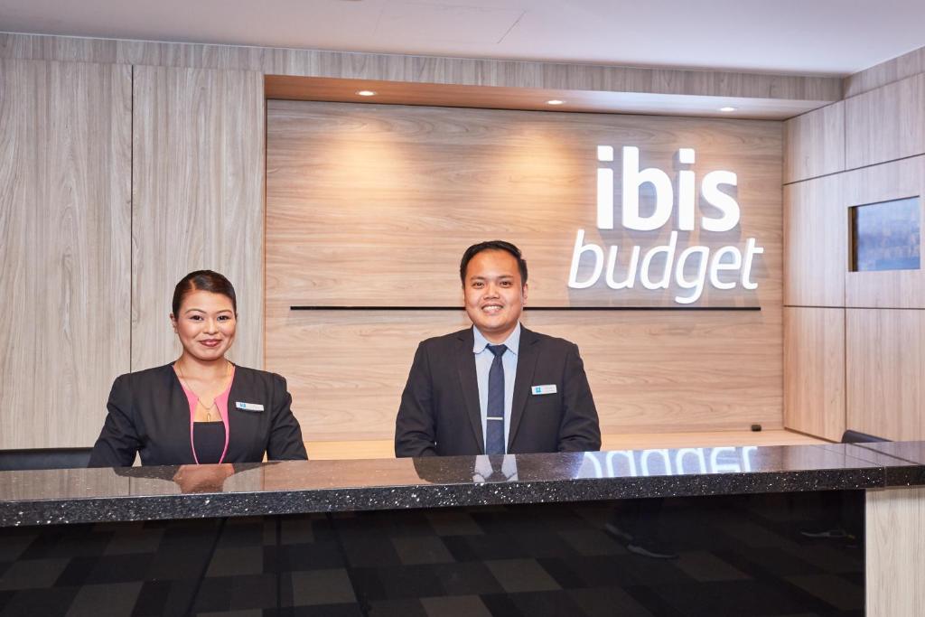 Ein Mann und eine Frau sitzen an einem Schreibtisch in einer Lobby. in der Unterkunft ibis budget Singapore Ruby in Singapur