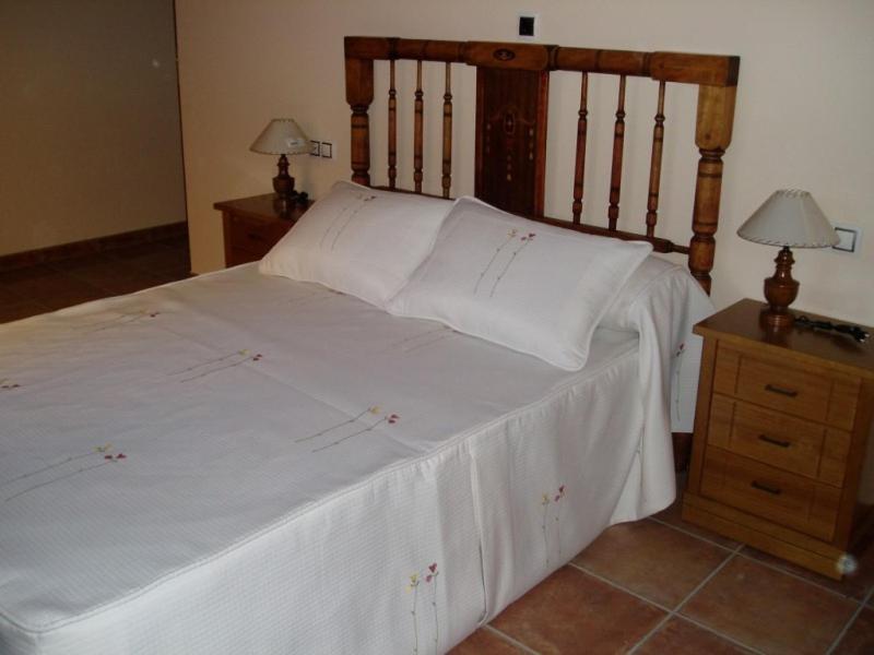 a large bed with white sheets and a wooden headboard at Hotel Restaurante el Horno in La Puebla de Valverde